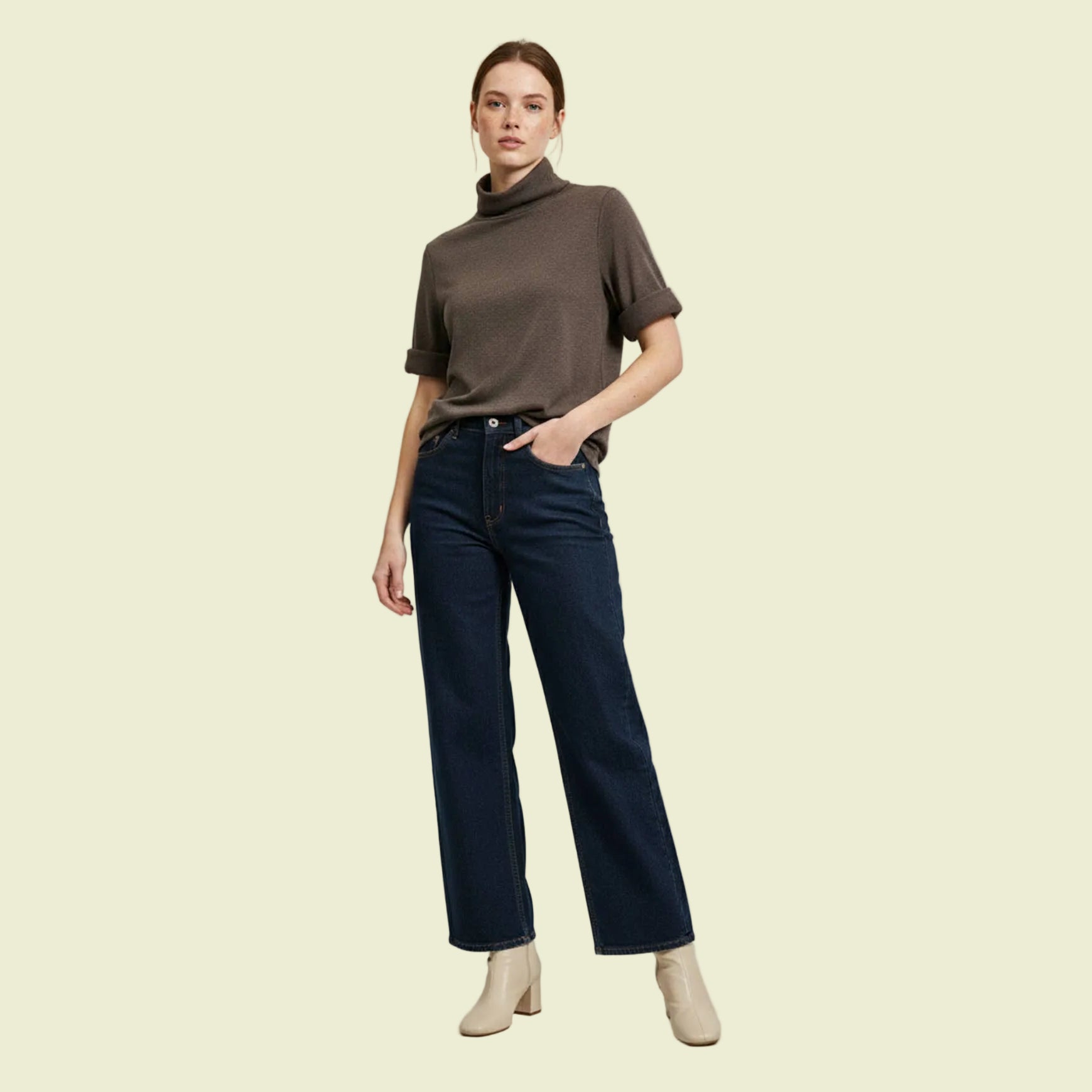 Woman wearing a brown turtleneck and dark blue jeans on a light gray background