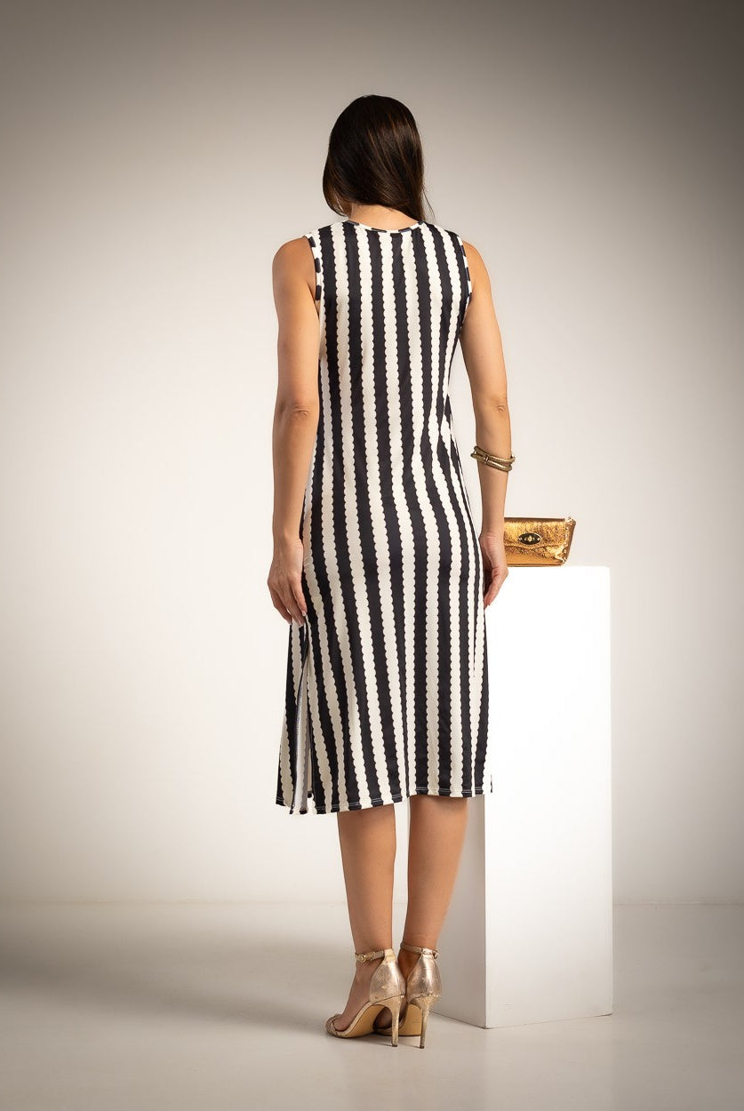 A woman stands with her back to the camera wearing a sleeveless black and white vertically striped midi dress