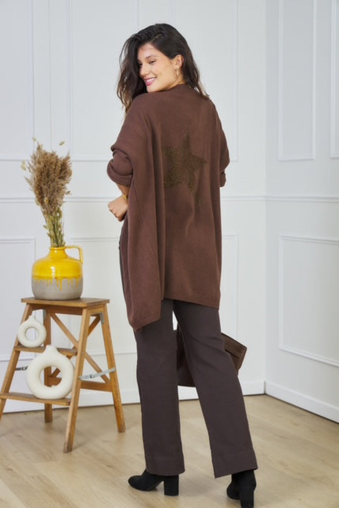 Woman wearing a brown cardigan with a star design in a room with a white wall and wooden floor.