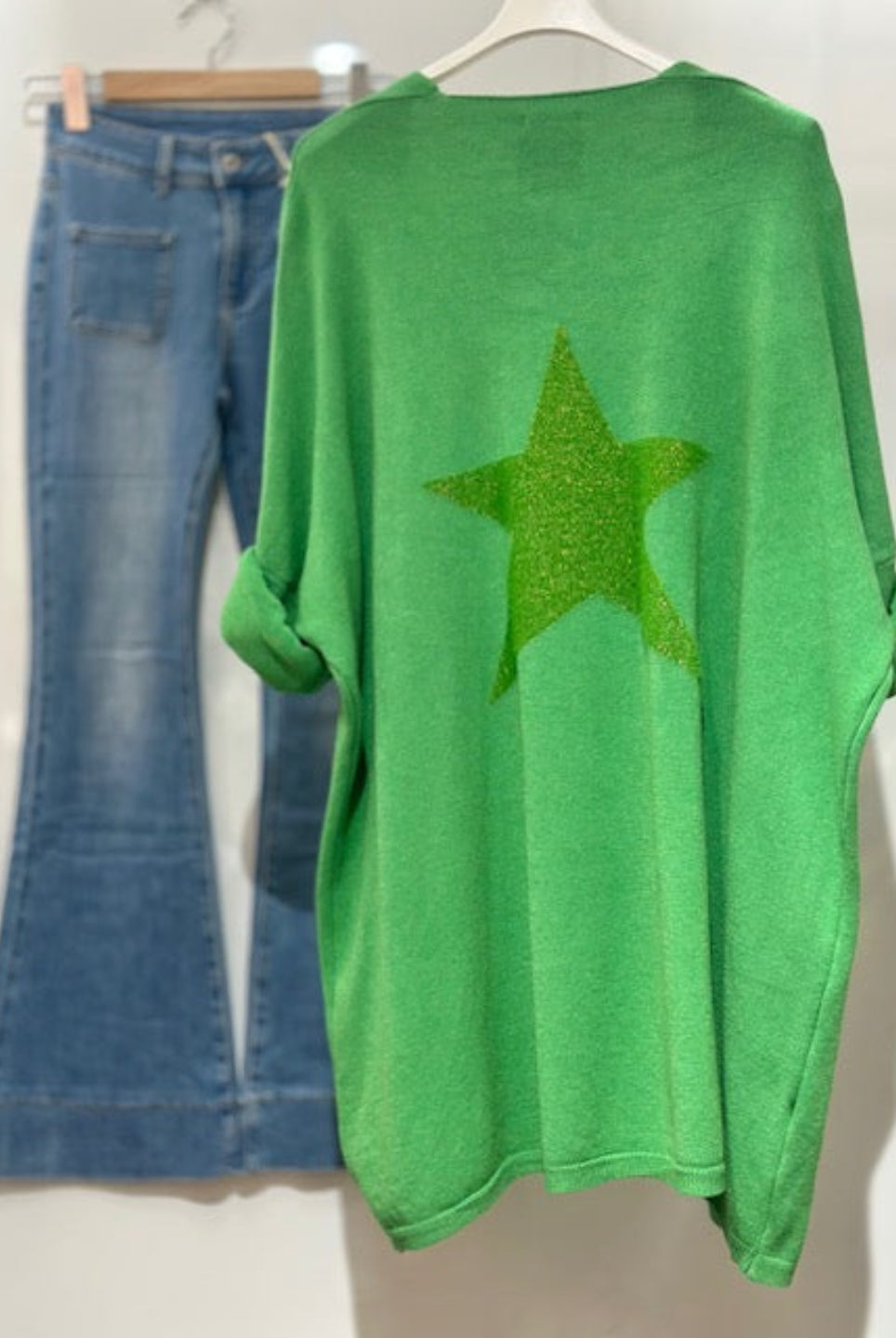 Green sweater with a star design and blue jeans on a white background