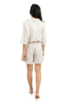 Person wearing a white outfit standing in front of a light green wall with a plant.