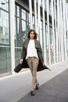 Woman walking outdoors wearing a long coat, white sweater, beige pants, and black shoes.