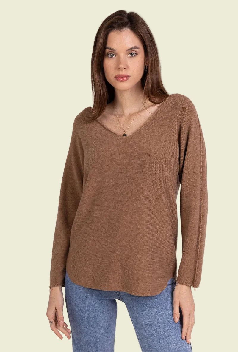 Woman wearing a brown long-sleeve top and blue jeans on a plain background