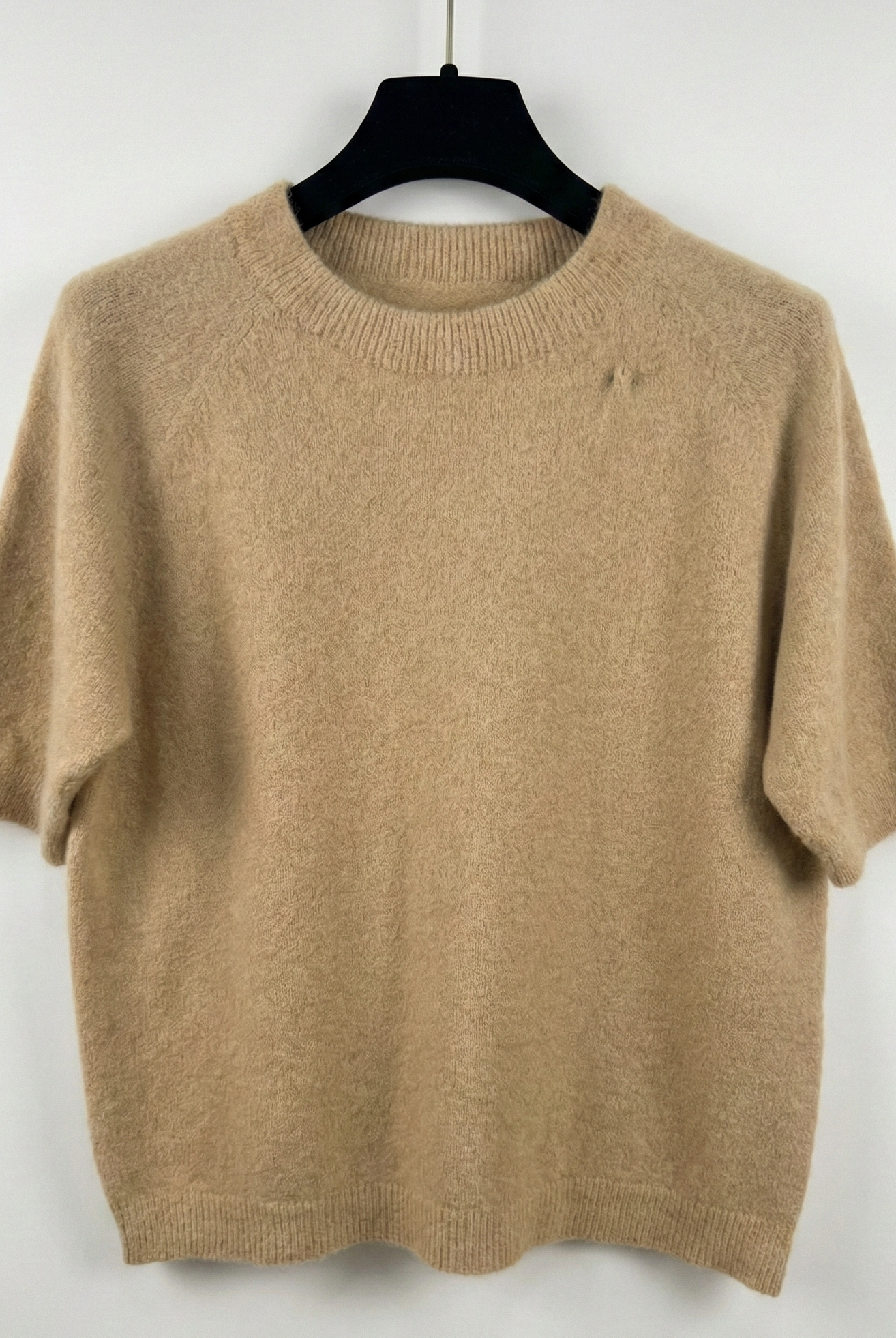 Beige sweater on a black hanger against a white background