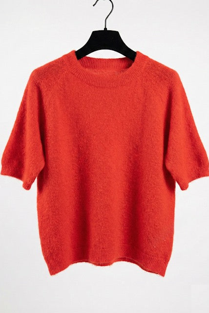 Orange sweater on a hanger against a white background
