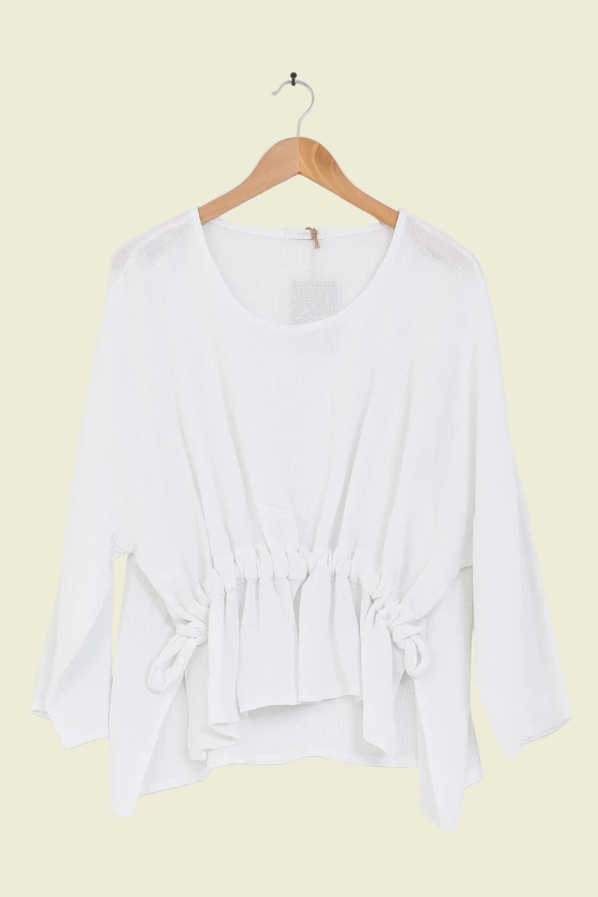 White linen tunic on a wooden hanger against a white background