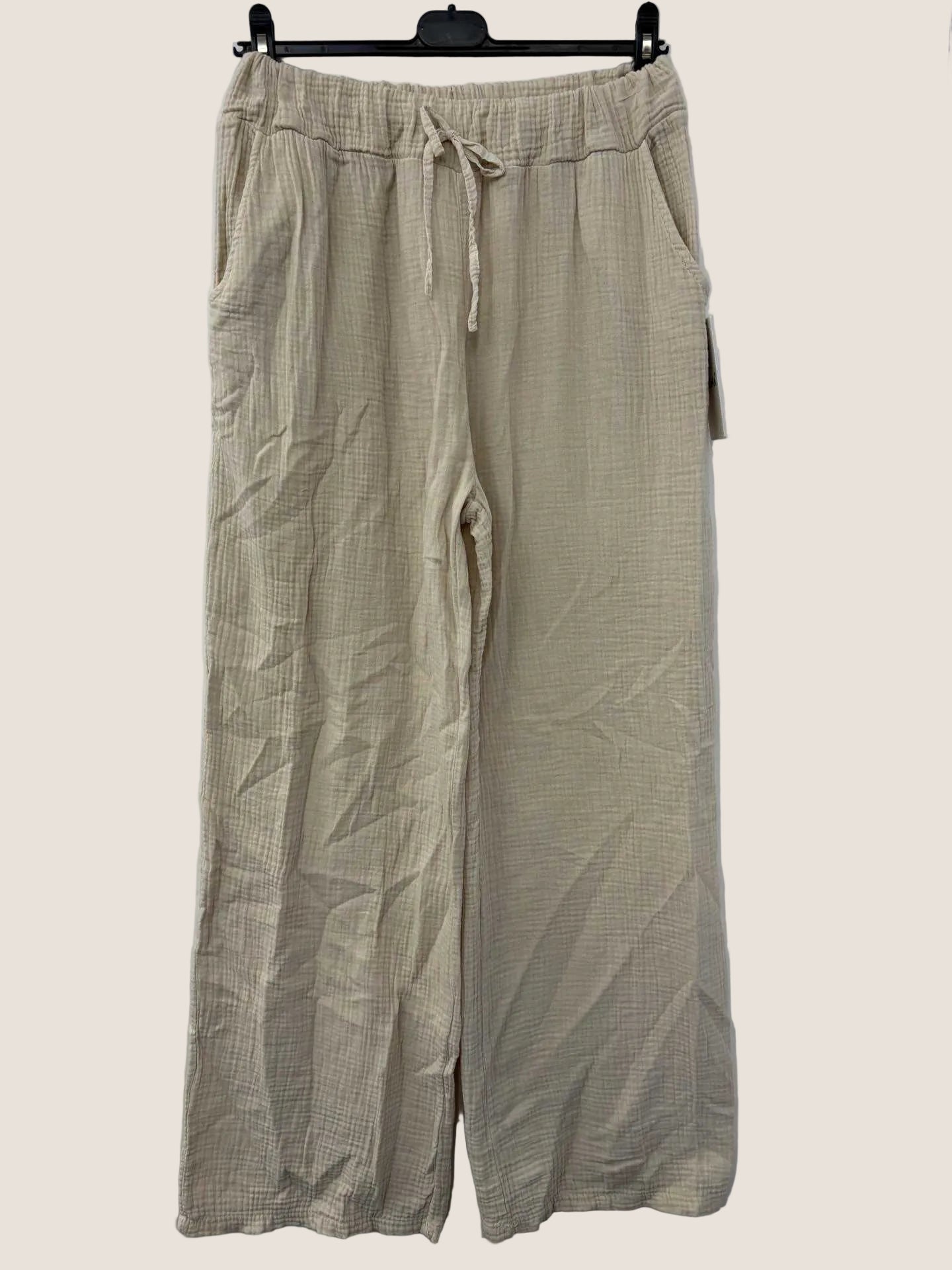 Beige cotton gauze pants on a hanger against a white wall