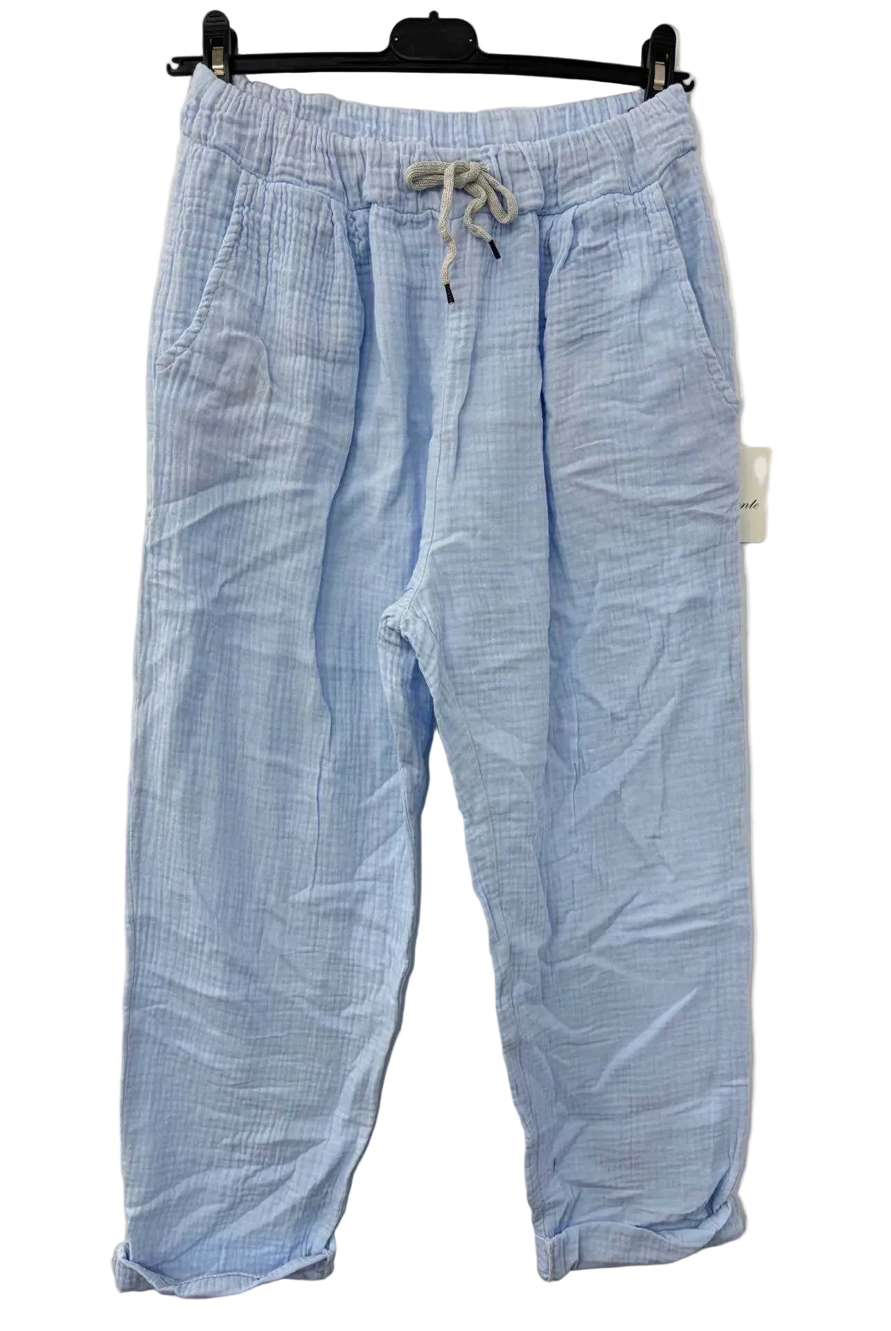 Sky Blue cotton gauze trousers on a hanger against a beige wall