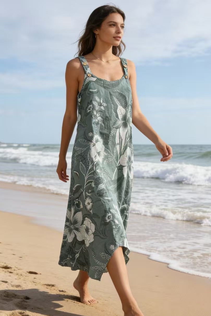 Woman in a green floral dress walking on a beach with ocean waves in the background