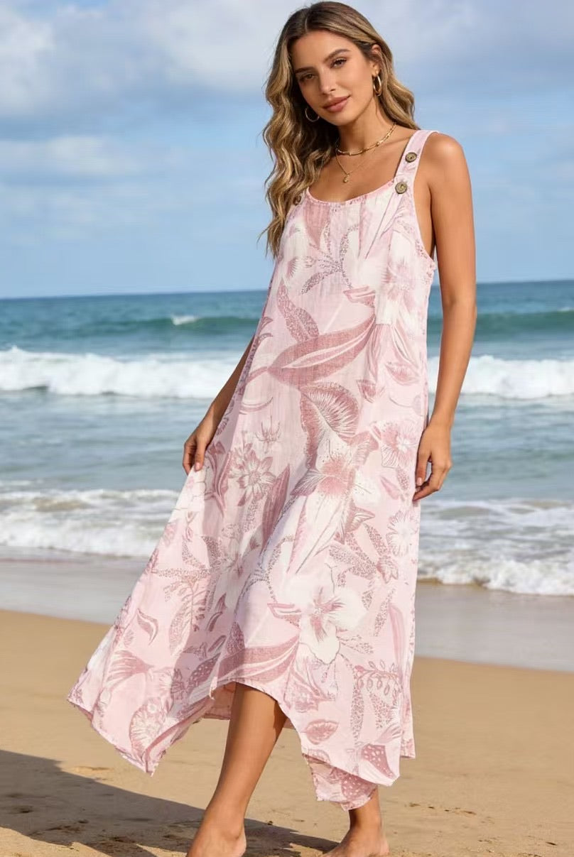 Woman in a pink floral dress standing on a beach with ocean waves in the background