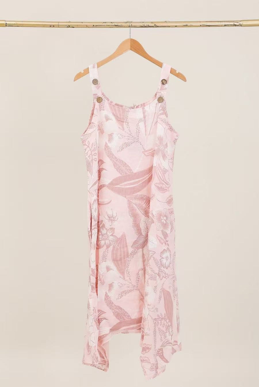 Pink floral dress hanging on a wooden hanger against a beige wall.