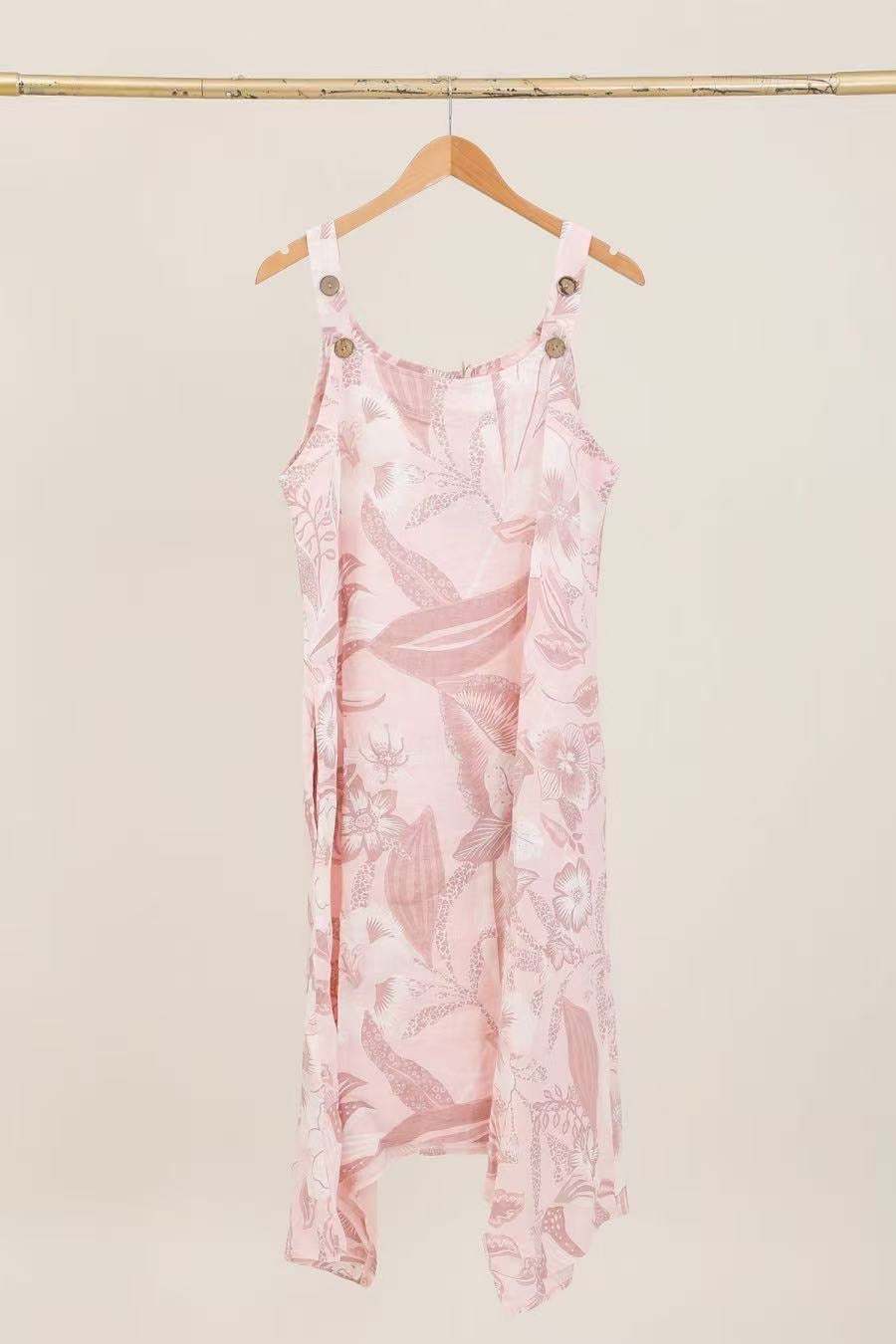 Pink floral dress hanging on a wooden hanger against a beige wall.