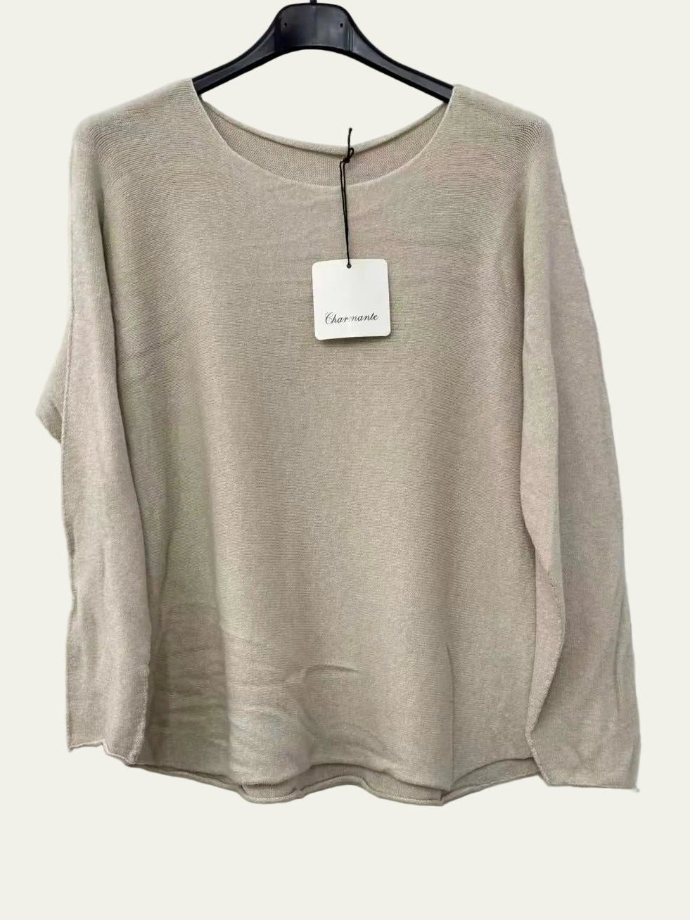 A light beige knit long-sleeve top hanging on a black hanger against a white wall,
