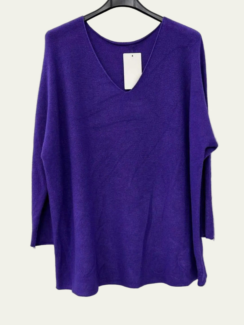 A purple knit long-sleeve top with a V-neck, hanging on a black hanger against a plain white wall.