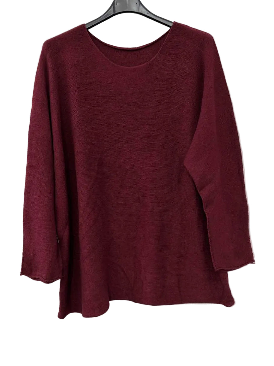 A long-sleeve crewneck knit top in deep burgundy, hanging on a black hanger against a plain off-white wall.