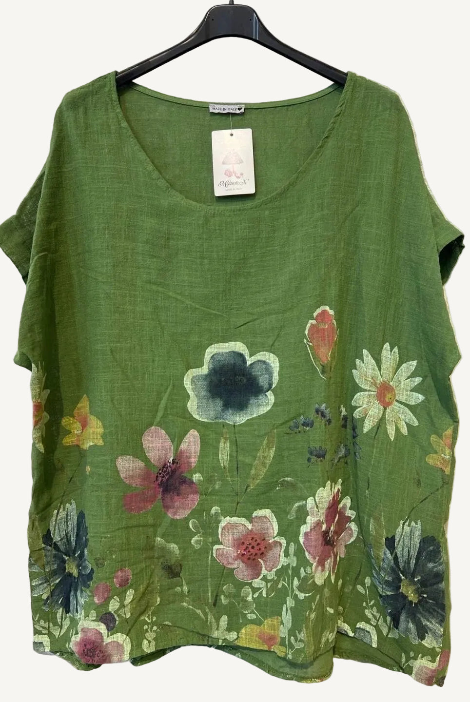 Green top with floral designs on a hanger against a textured white background