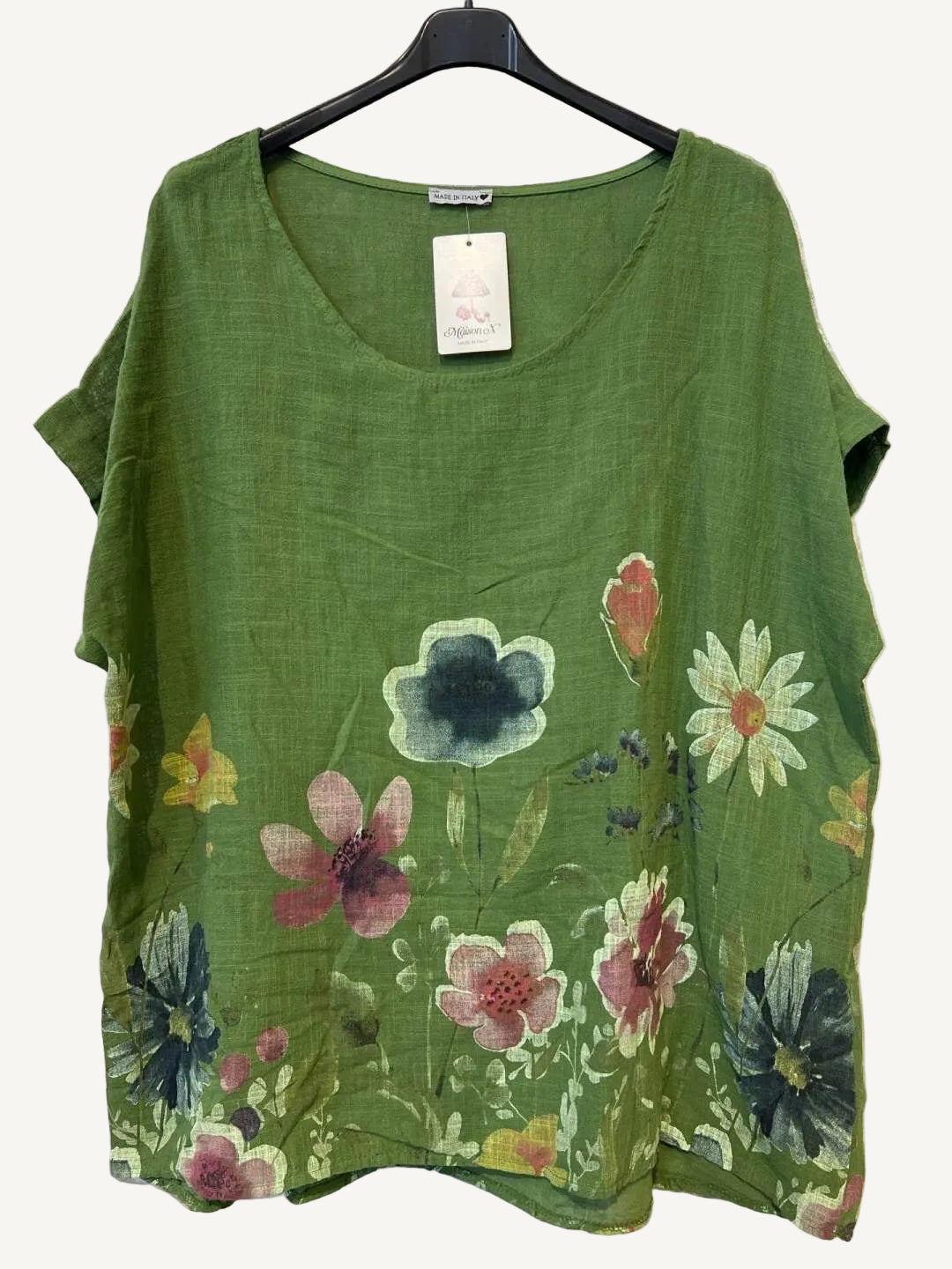 Green top with floral designs on a hanger against a textured white background