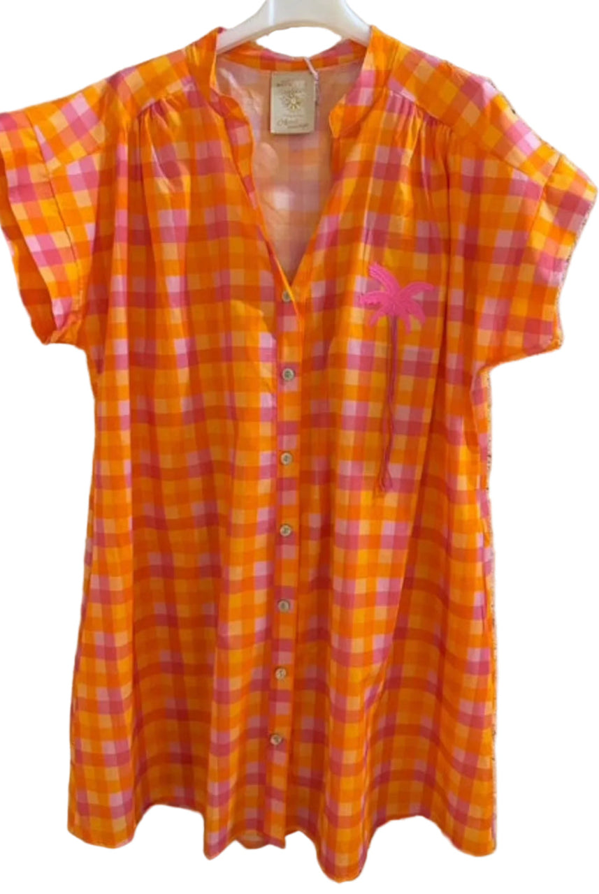 Orange and pink checkered shirt dress on a hanger against a textured wall.
