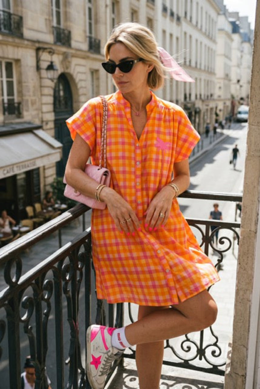 Woman in an orange checkered dress standing on a balcony in an urban setting