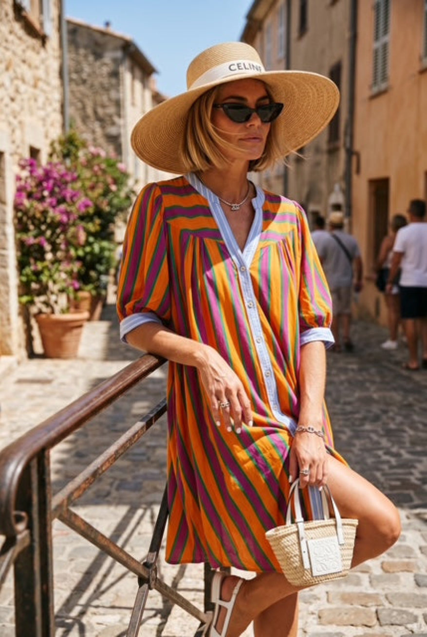 Woman in a colorful striped dress and sun hat walking down a street.
