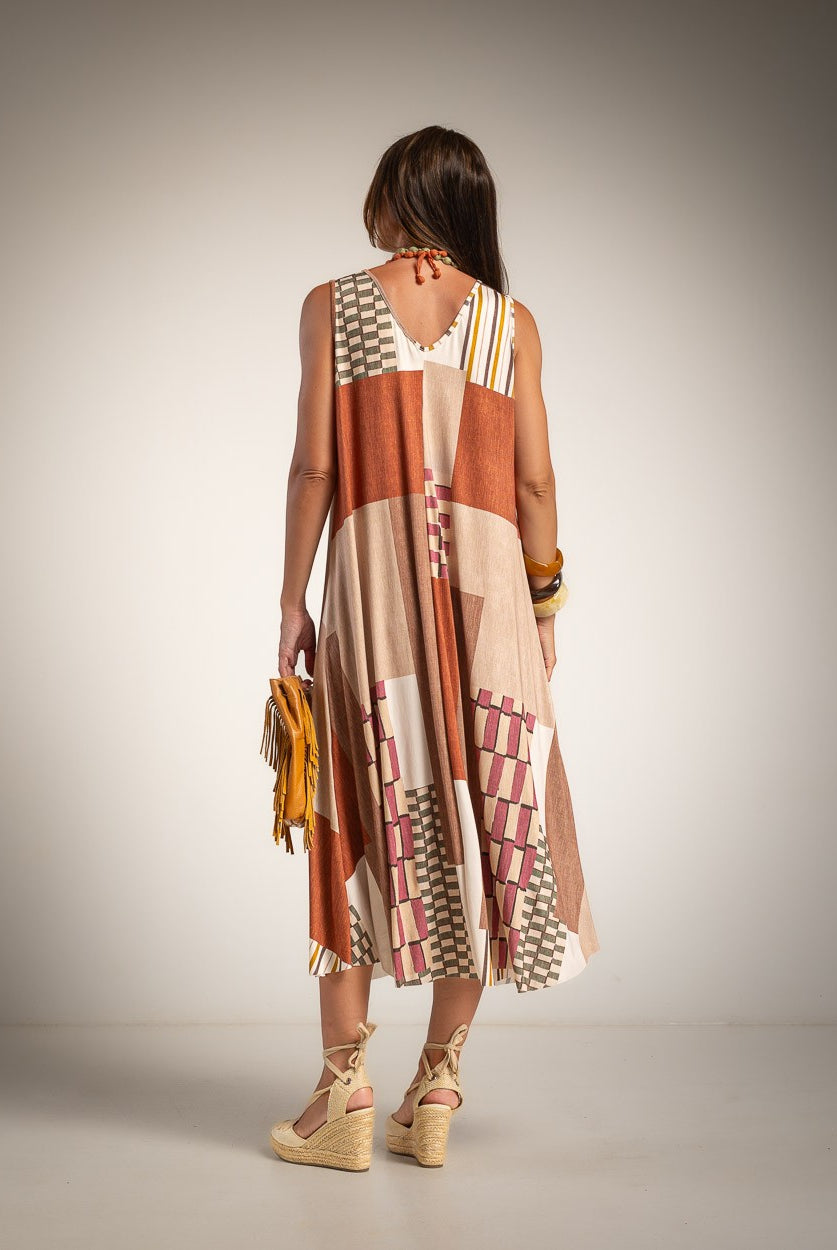 A woman is shown from behind wearing a sleeveless patchwork midi dress with geometric patterns in beige, rust orange, and white.