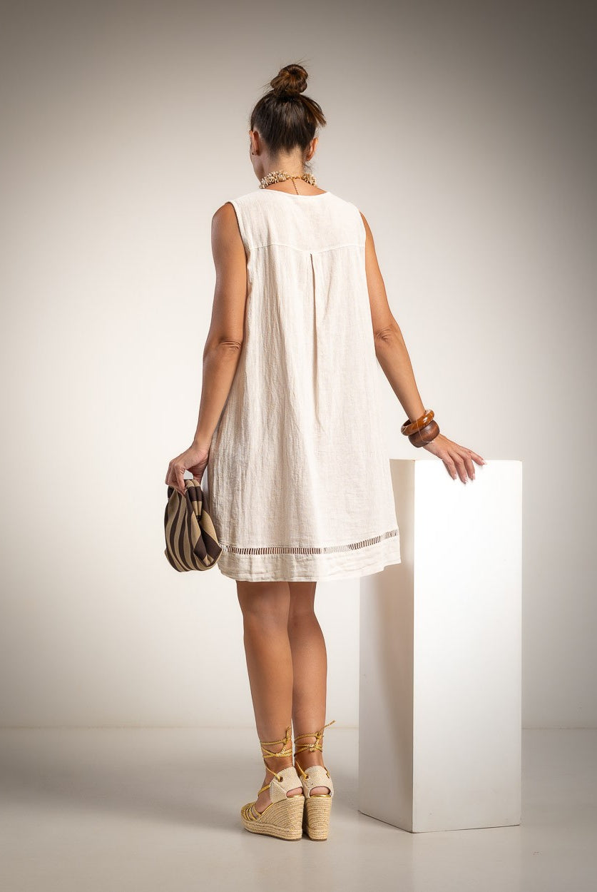 A woman stands with her back to the camera wearing a sleeveless beige dress with ladder detail