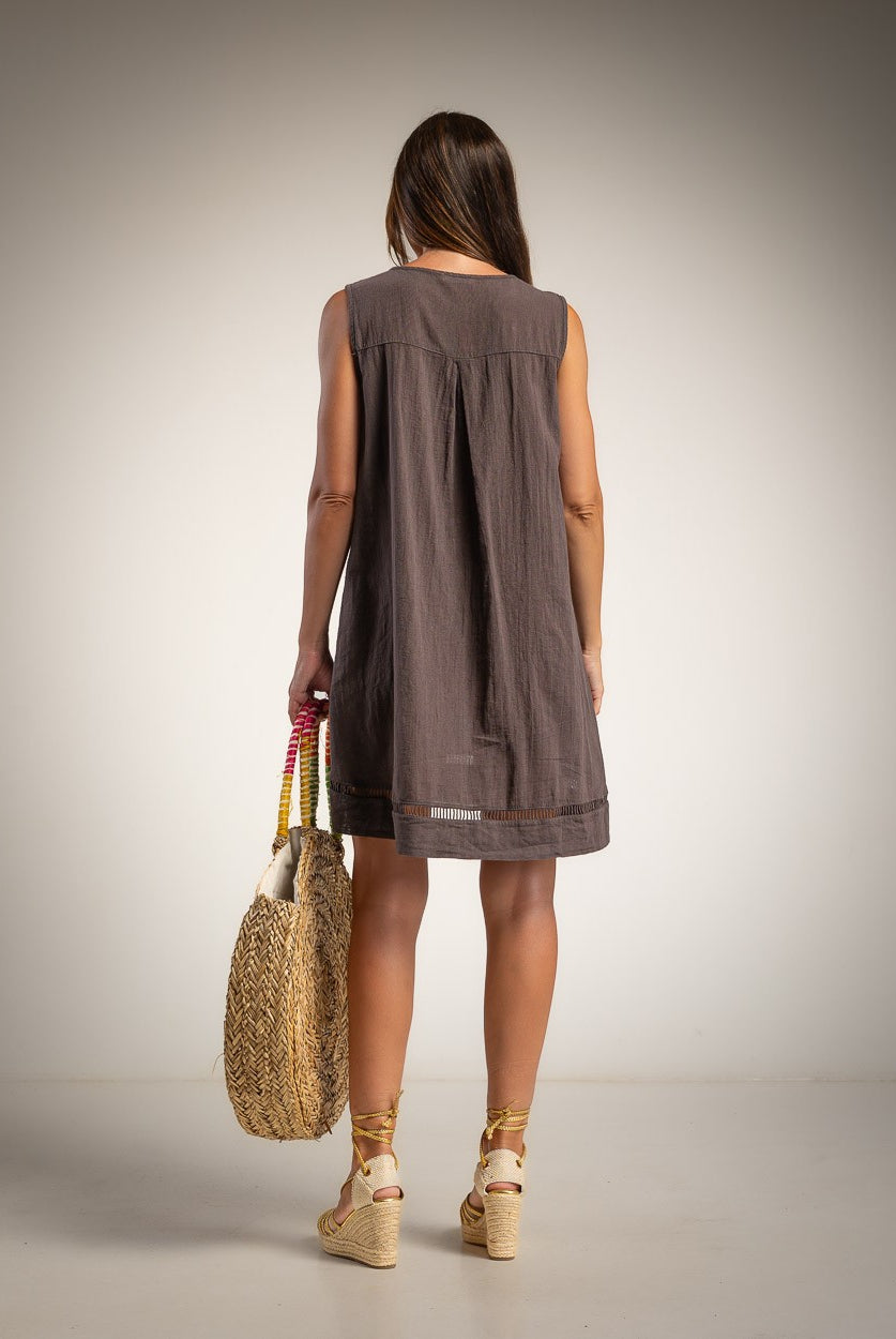 A woman viewed from behind wearing a sleeveless brown dress, holding a woven straw tote bag