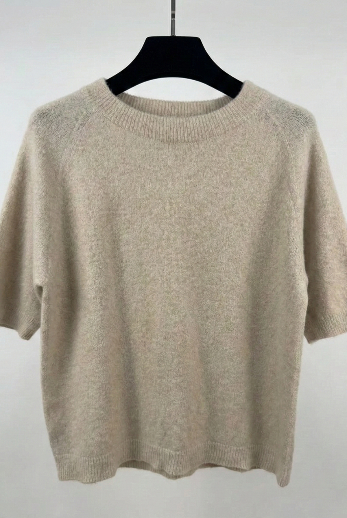 Beige sweater on a black hanger against a white background