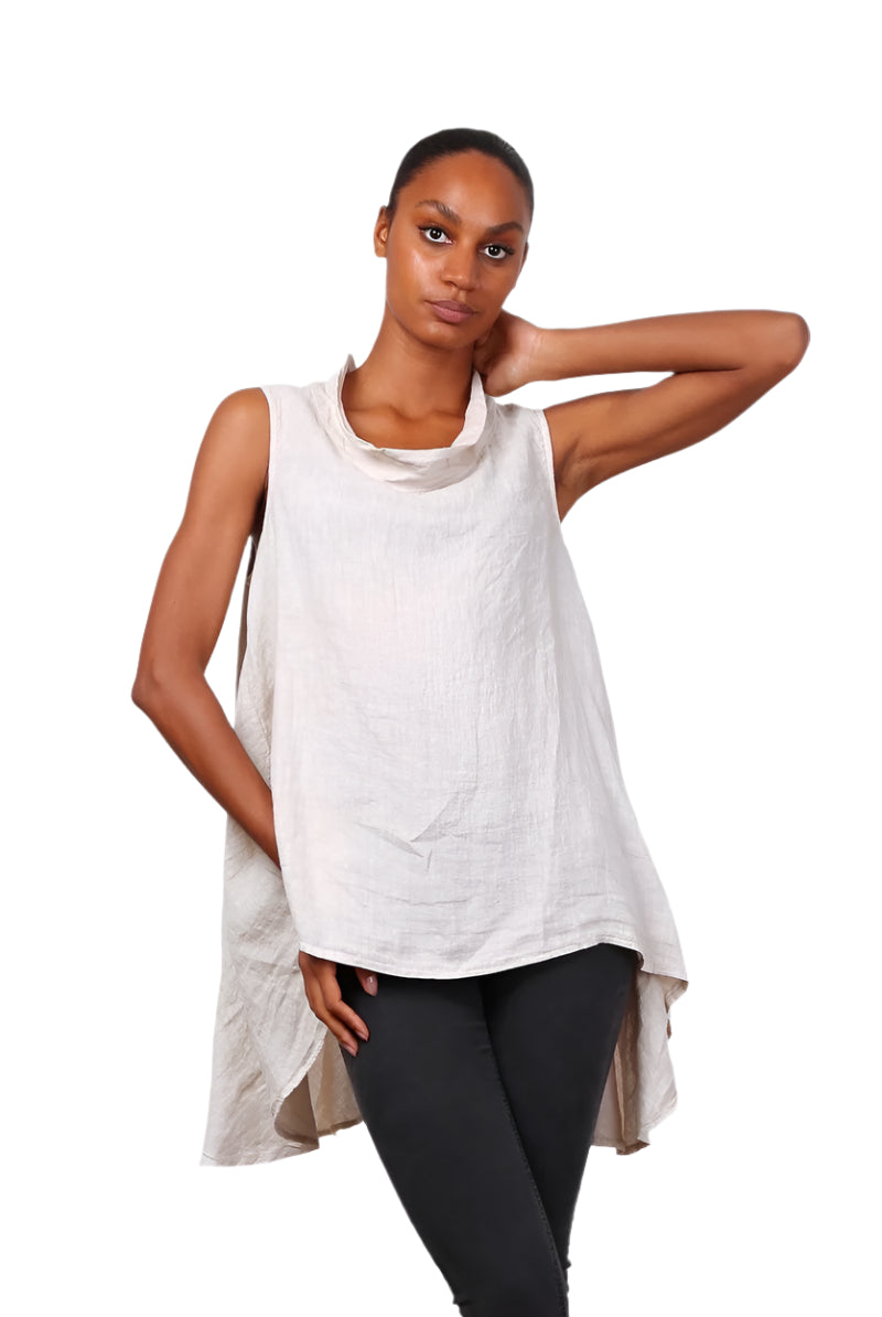 A woman wearing a beige sleeveless cowl neck top with an asymmetrical hem, paired with white trousers.