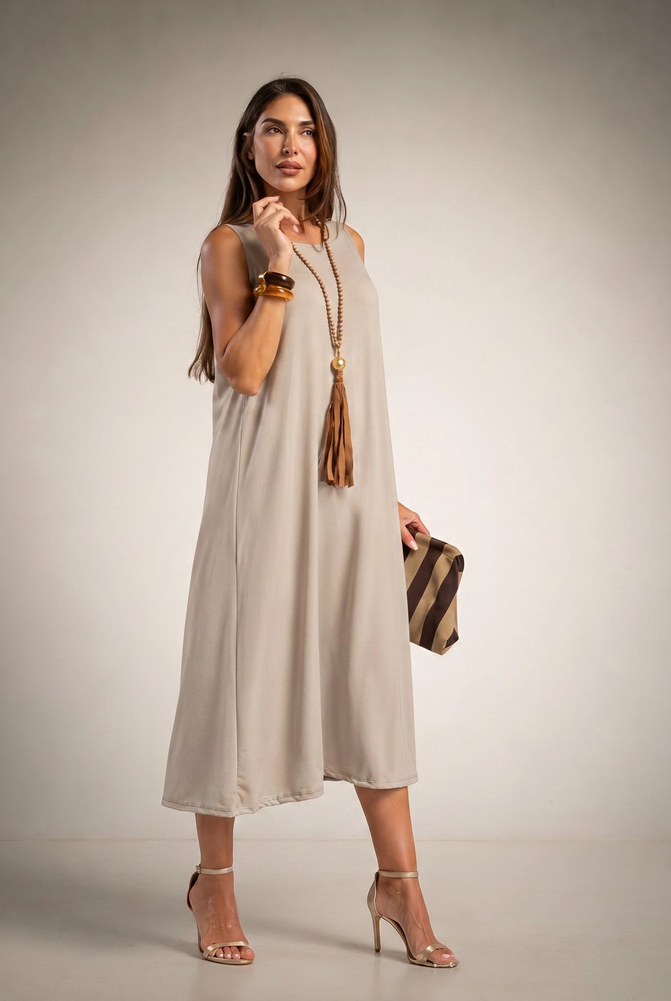 A woman models a sleeveless, midi-length beige dress with a relaxed, flowy silhouette.