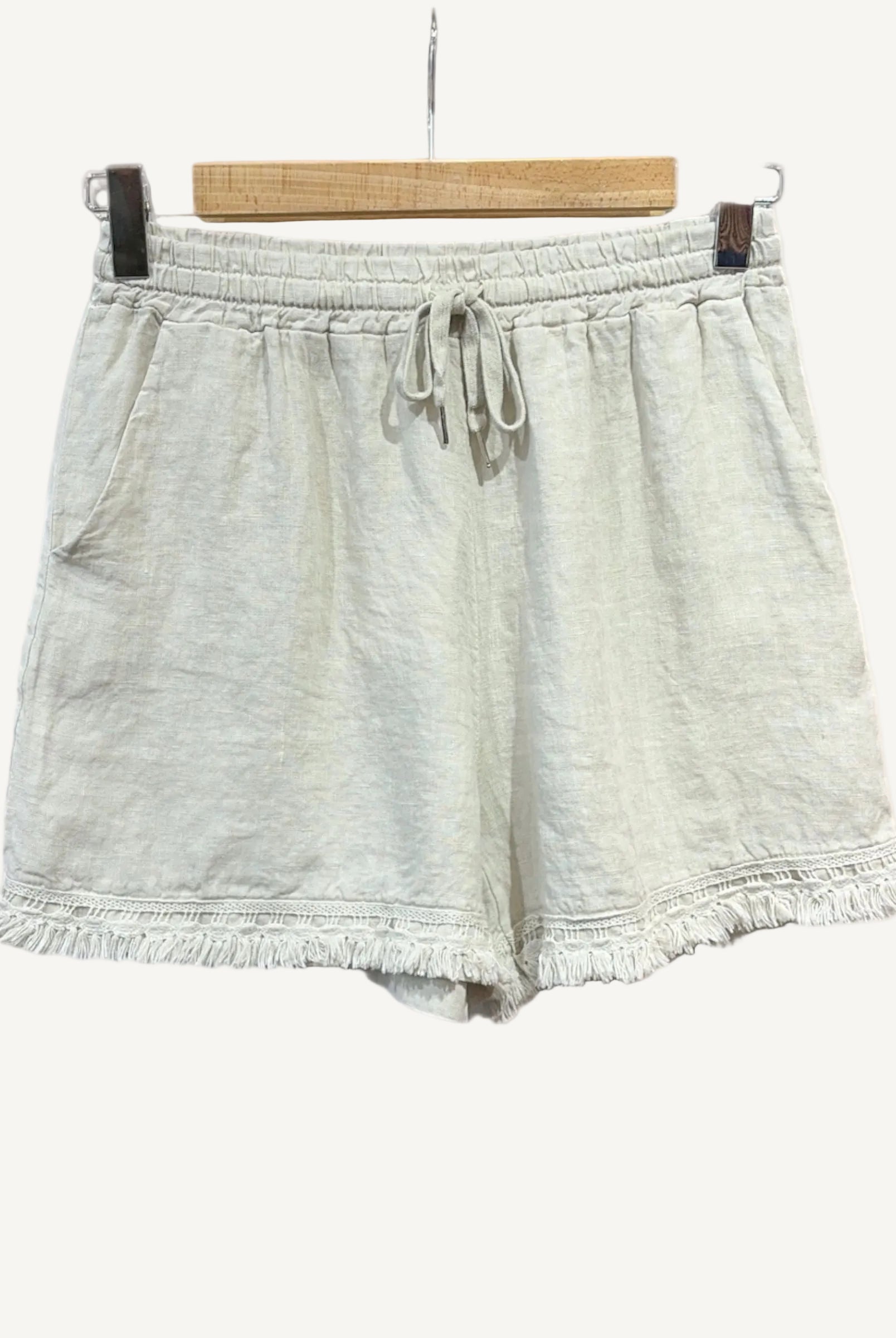 Beige shorts with frayed edges on a hanger against a white background