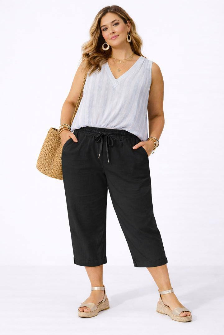 Woman wearing a white sleeveless top and black pants, standing against a white background.