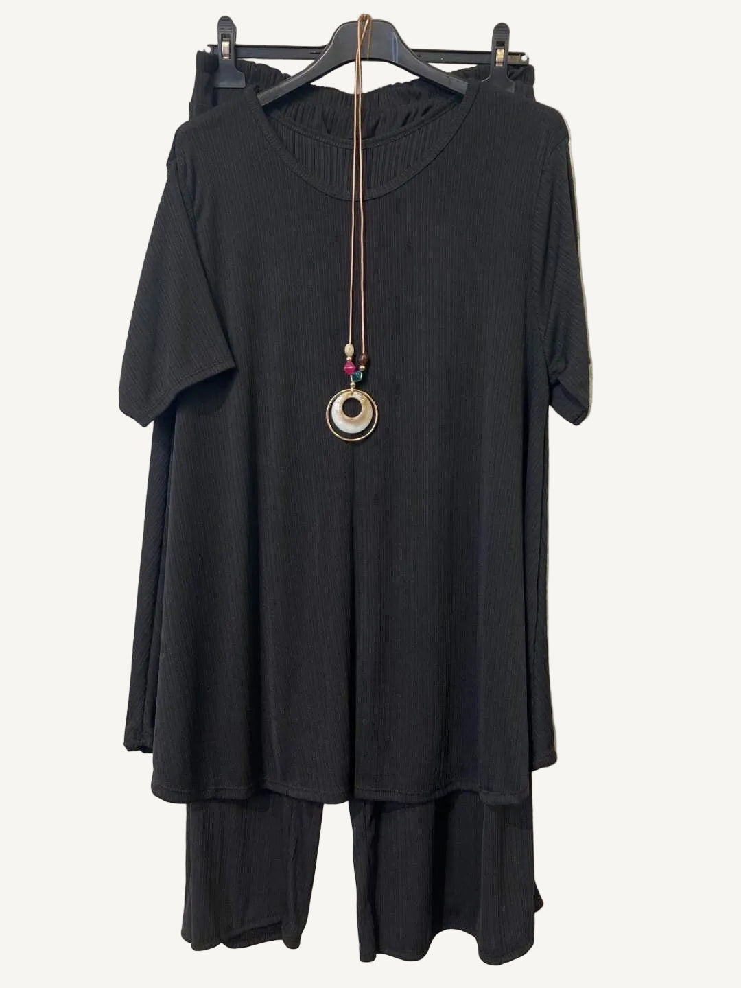 Black outfit with a necklace on a hanger against a textured white background