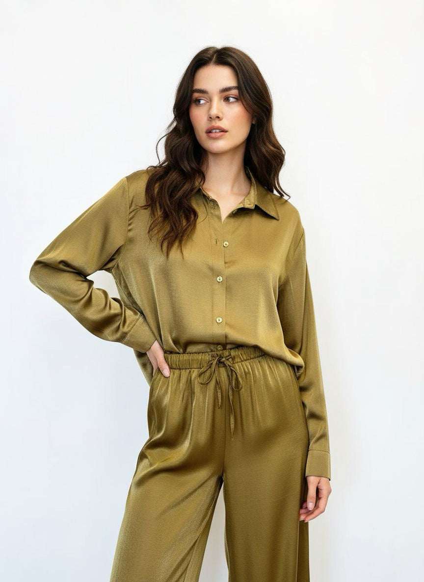 A woman modeling a matching olive green satin button-up shirt and wide-leg drawstring pants set against a plain white studio background.