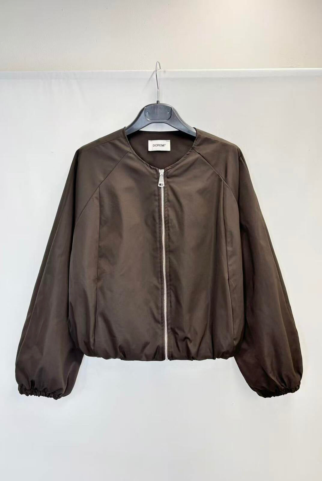 A dark brown zip-up jacket hanging on a black hanger against a plain white wall.