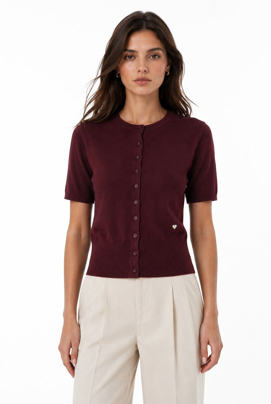 A woman modeling a short-sleeve burgundy knit top with a button-down front, paired with cream-colored trousers, against a plain white background.