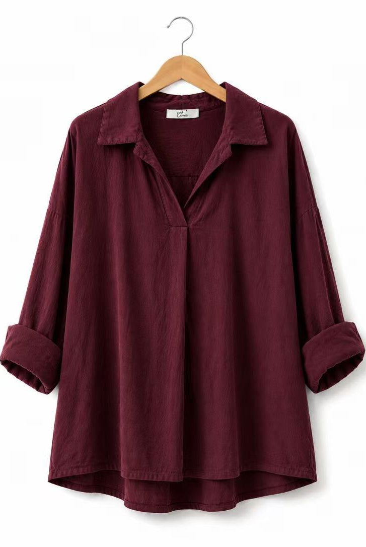 A dark burgundy long-sleeve shirt with a relaxed fit, a collar, and rolled cuffs, hanging on a wooden hanger against a plain white background.