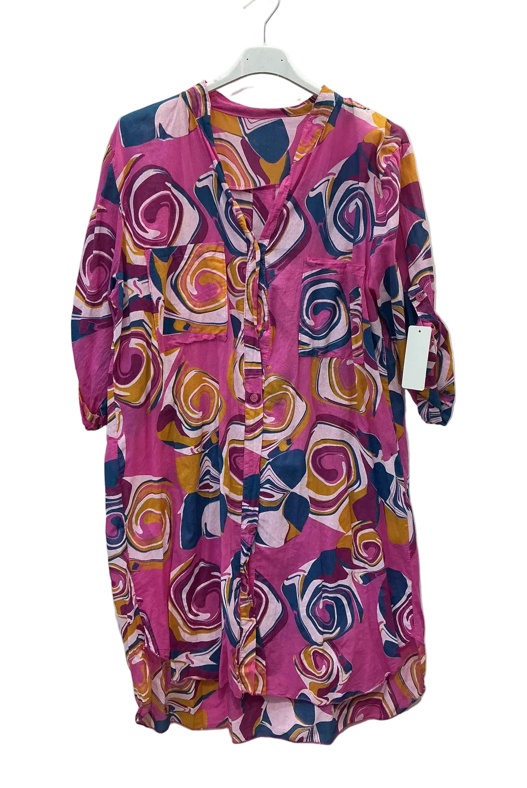 A pink long-sleeve tunic dress with a bold abstract swirl pattern in yellow, orange, navy, and white, hanging on a white hanger against a plain white wall.