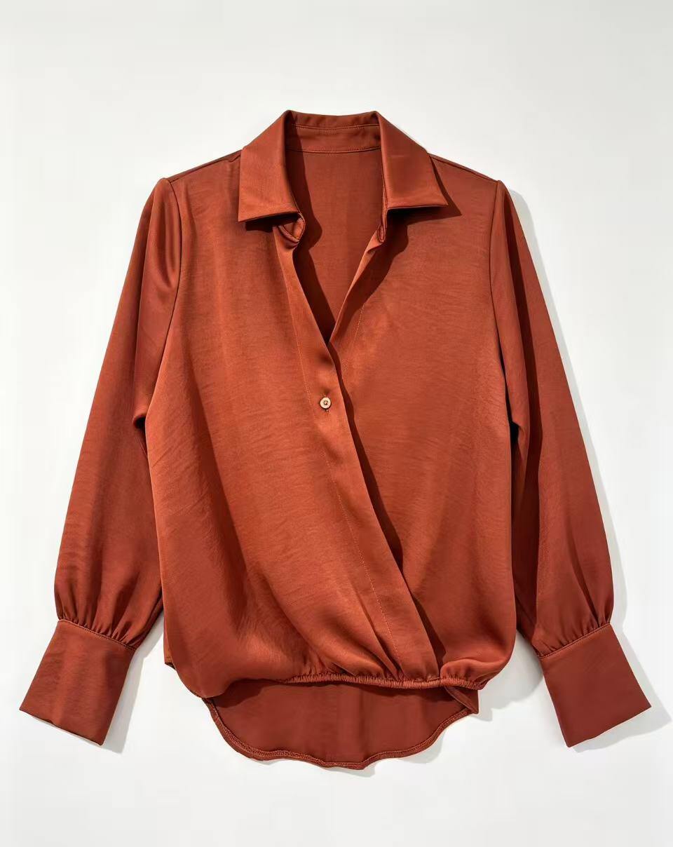 A rust-orange long-sleeve blouse with a pointed collar, button front, and gathered cuffs, laid flat against a light off-white background.