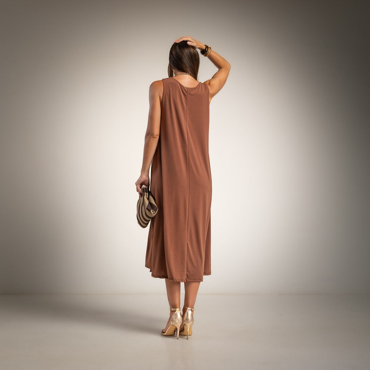 A woman is shown from behind wearing a sleeveless, brown midi dress