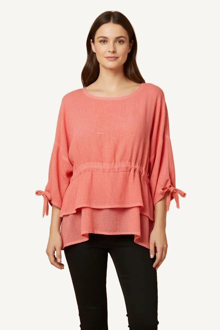 Woman wearing a coral pink layered top against a beige background