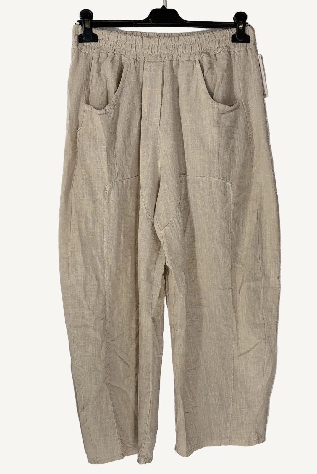 Beige pants hanging on a hanger against a textured white wall
