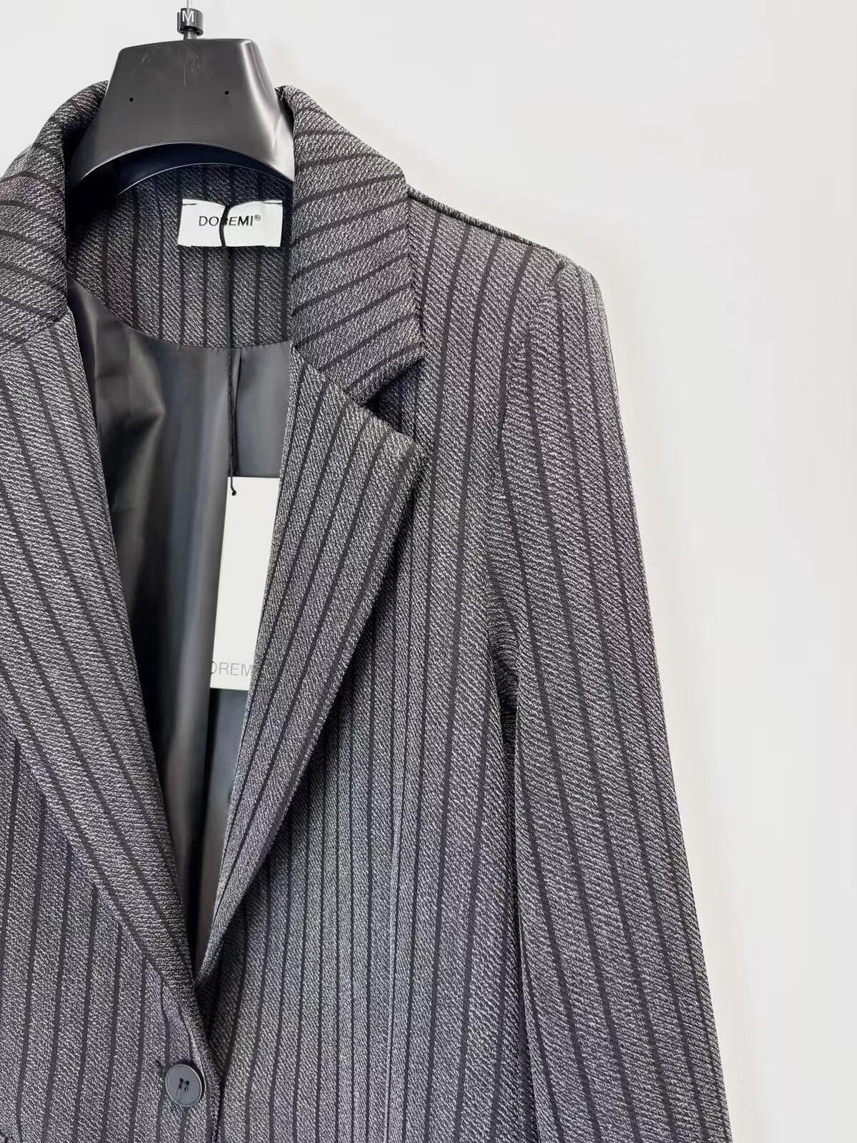 A close-up of a grey pinstripe blazer hanging on a black hanger against a plain white background.