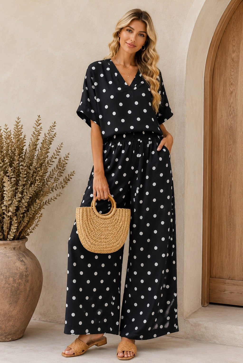 Woman wearing a black polka dot jumpsuit standing in front of a wooden door.