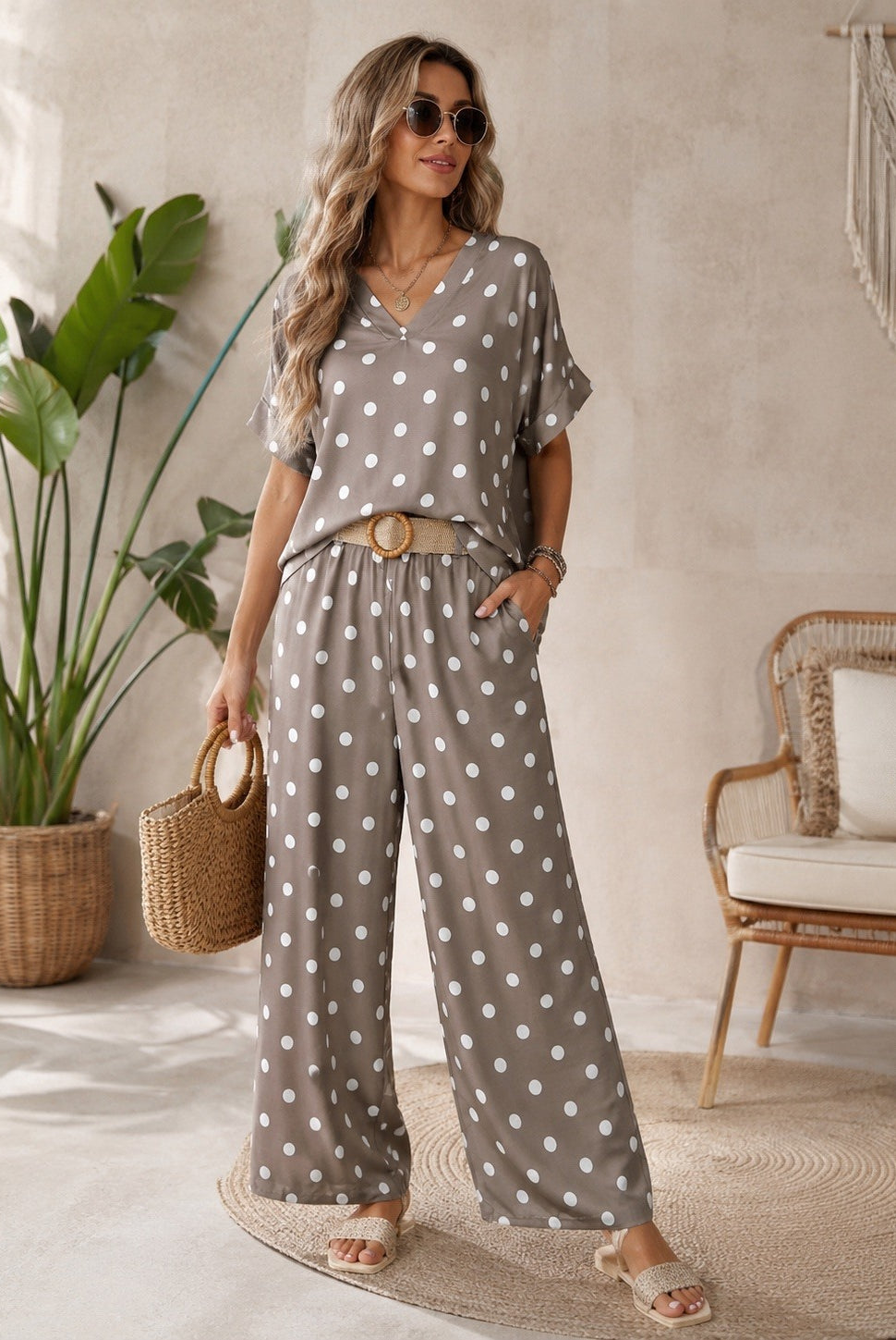 Woman in a polka dot outfit standing in a room with plants and a chair.