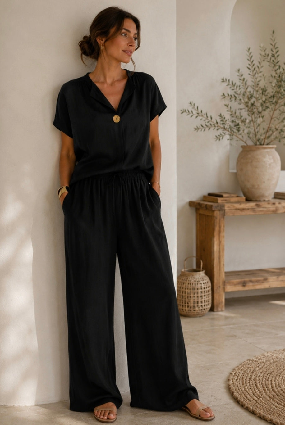 Woman wearing a black outfit standing in a room with a wooden table and plants.