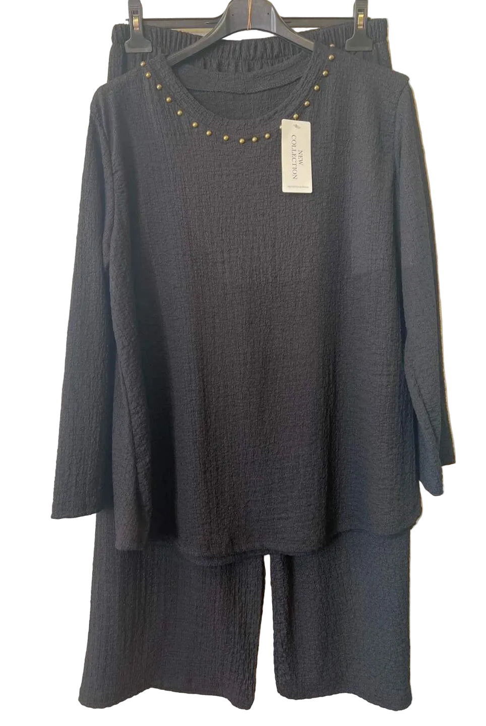 A black textured two-piece set consisting of a long-sleeve top with gold stud detailing around the neckline and matching wide-leg pants