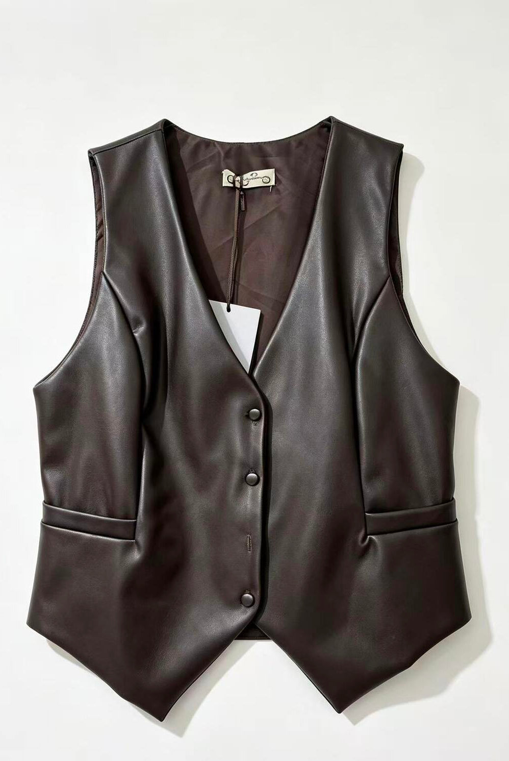 A dark brown faux-leather vest with a V-neck, button-front closure, and side pockets, laid flat against a light off-white background.