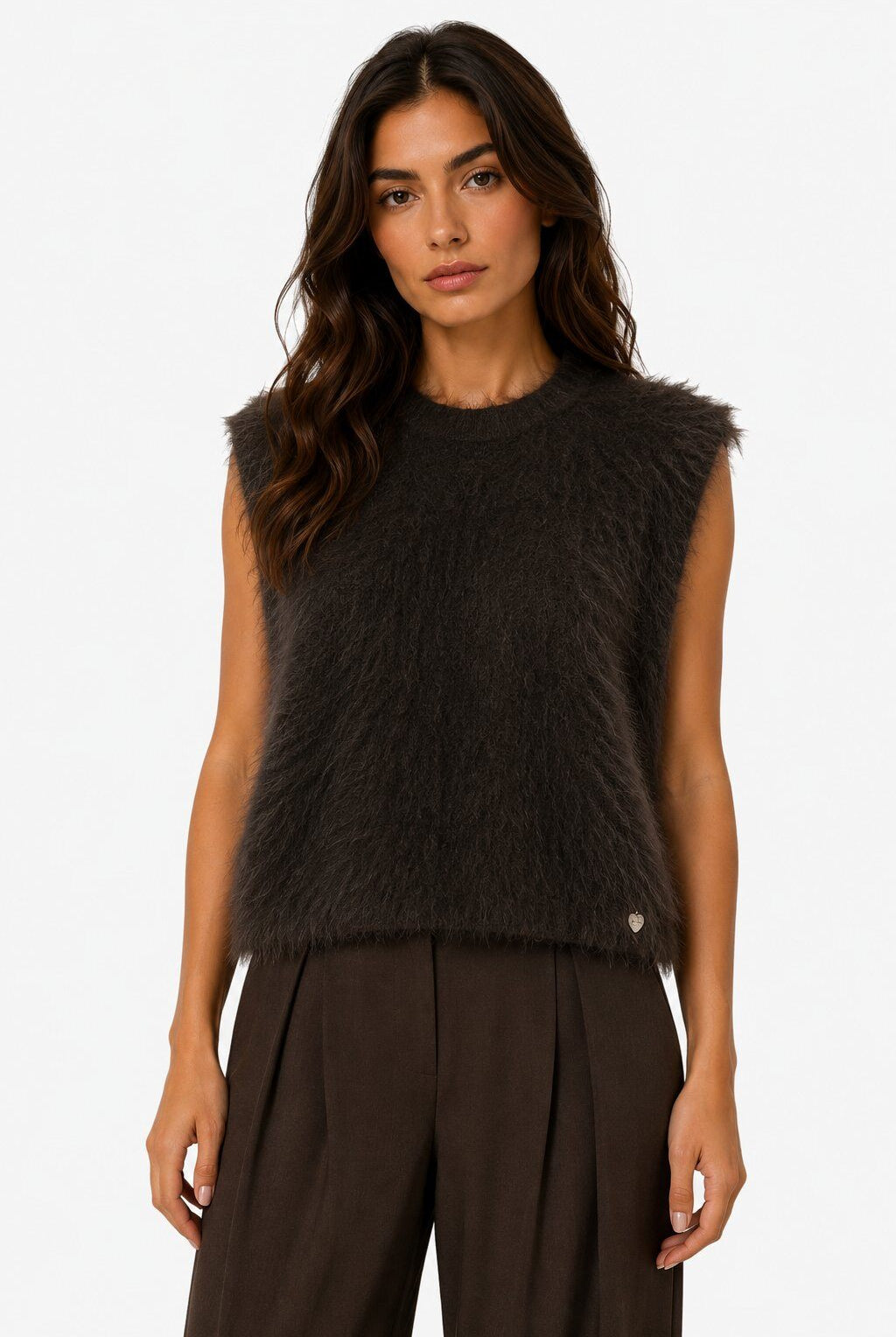 A woman modeling a sleeveless, dark brown fuzzy knit vest with a small gold button detail on the lower right, paired with dark brown wide-leg trousers, against a plain white background.