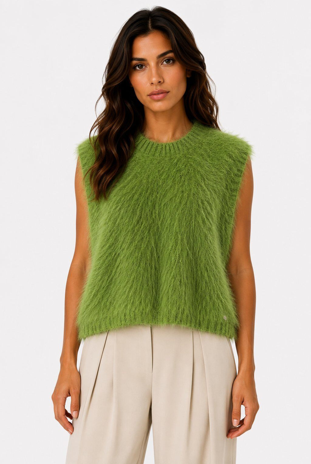A woman modeling a sleeveless, fuzzy lime green knit sweater vest paired with light beige trousers, set against a plain light gray studio background.